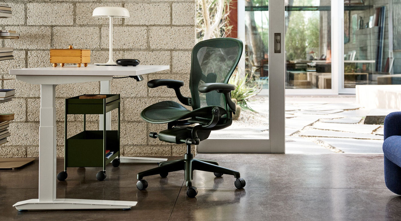 Jasper-vihreä Herman Miller Aeron -työtuoli osana valoisaa kotitoimistoa, jossa on valkoinen Jarvis-seisomapöytä ja oliivinvihreä OE1-säilytysvaunu.