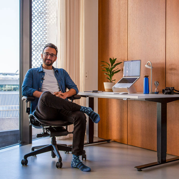 Valokuva podcastaaja Ali Abdaalista istumassa grafiitinvärisessä Herman Miller Aeron -työtuolissa Nevi-seisomapöydän edessä, jossa on mustat jalat ja valkoinen pöytälevy sekä kannettava tietokone Oripura-kannettavan telineessä