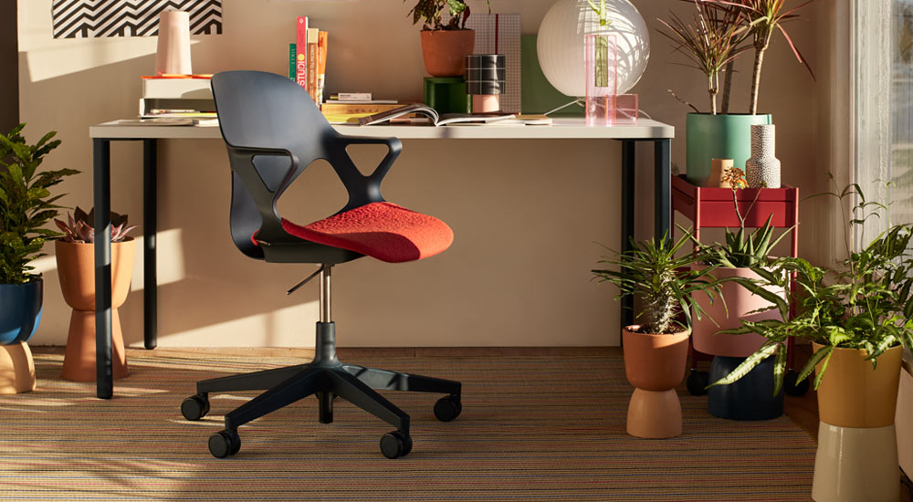 Musta Zeph-työtuoli punaisella istuintyynyllä on sijoitettu Herman Miller OE1 -työpöydän eteen. Sijoitettu kotitoimistoympäristöön, jossa on punainen OE1-vaunu ja valikoima sisäkasveja värikkäissä ruukuissa.