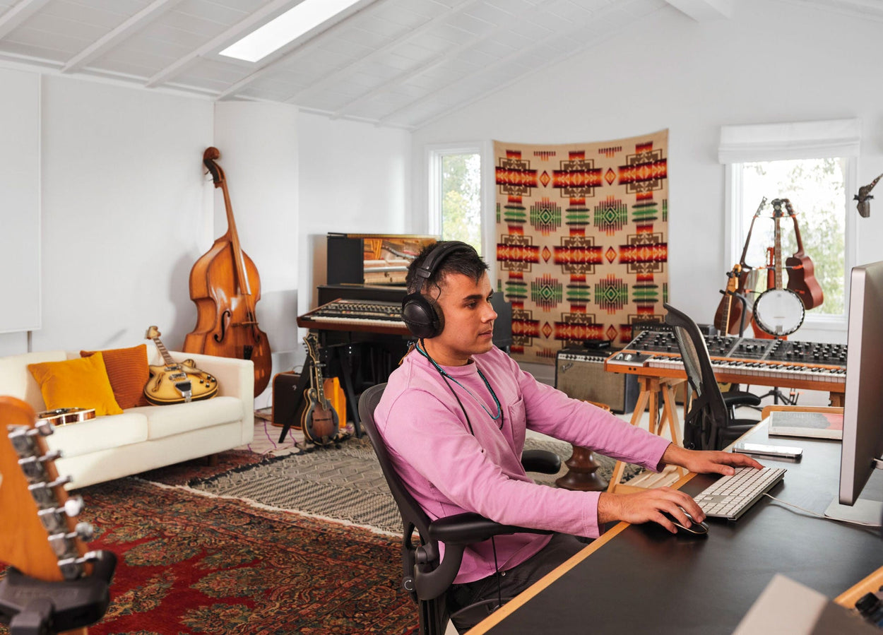 Rostam, muusikko, tuottaja ja säveltäjä, istuu grafiittivärisessä Aeron-työtuolissa tietokoneen ääressä kuulokkeet päässä, taustalla musiikki-instrumentteja.